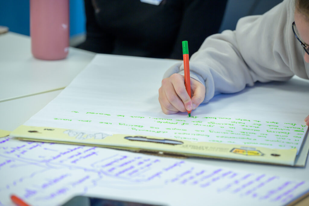 Young person writing on a large piece of white paper with green pen