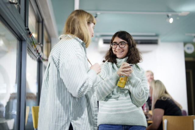 Two women talking. One woman is holding a bottle of juice.